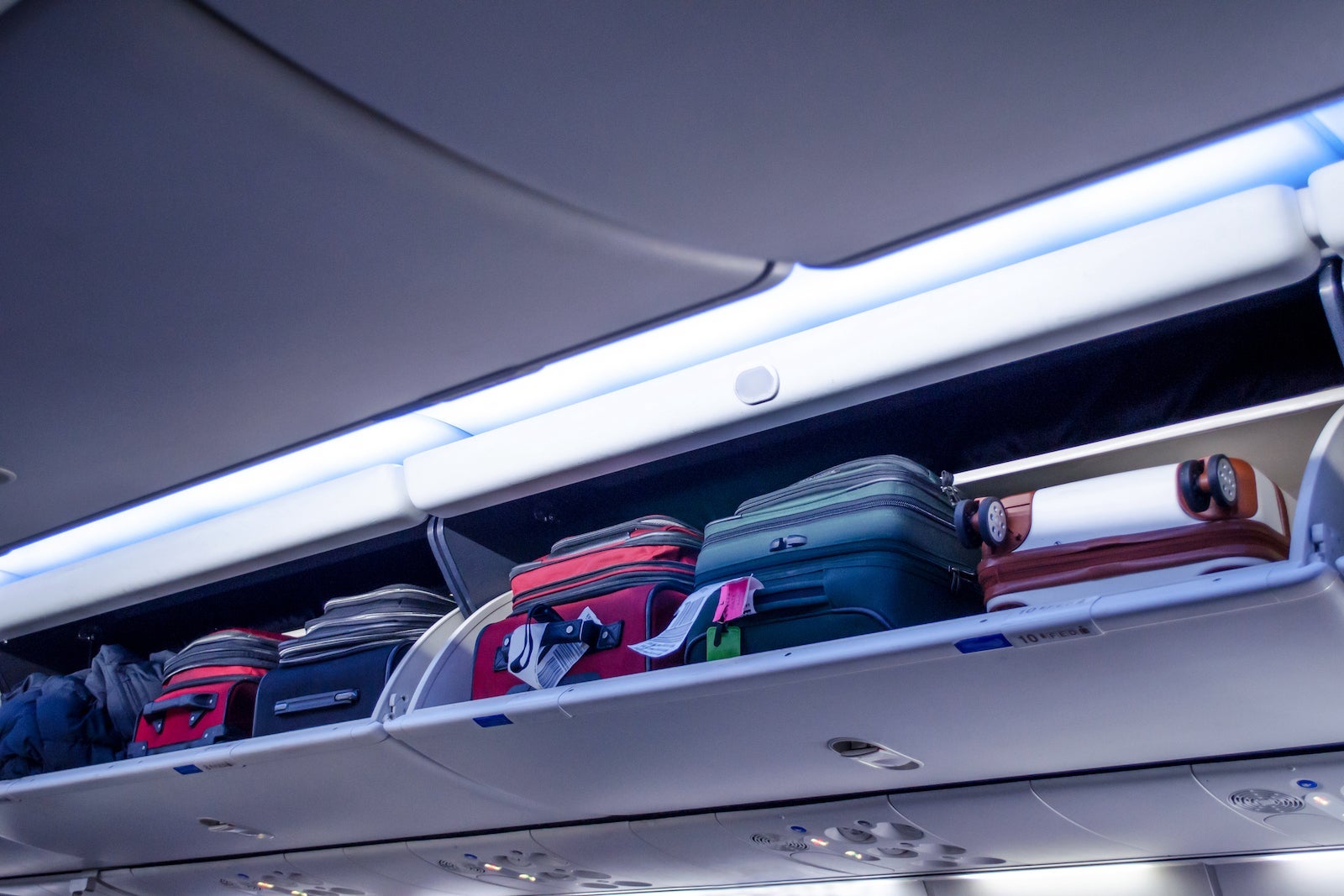 Carry On Bags Are Stuffed In An Overhead Luggage Compartment On An Airplane