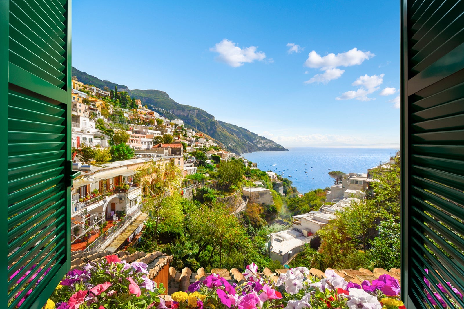 Mountain, city and sea view through an open window with shutters of the city of Positano on the Amalfi Coast of Southern Italy during summer.