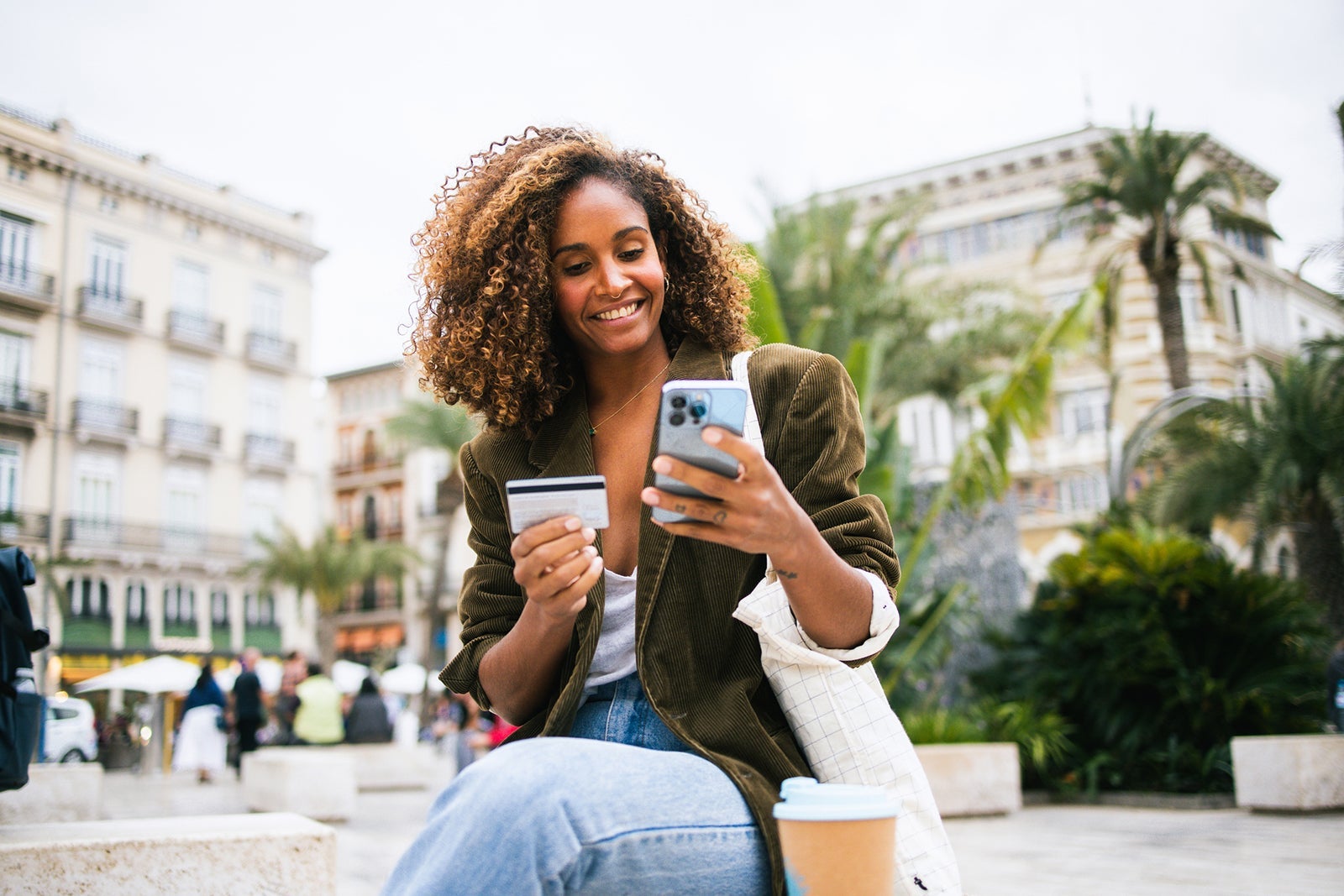 Happy woman enjoying coffee on the street and shopping online