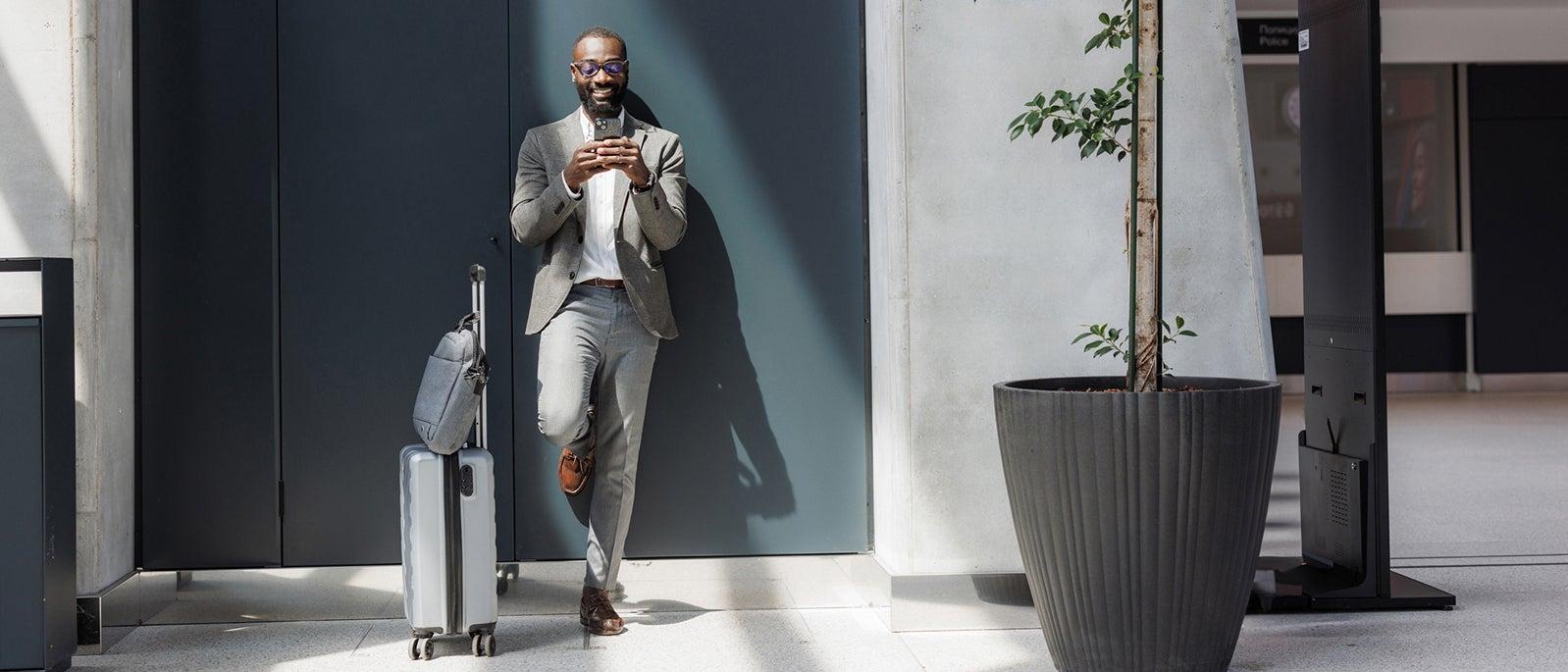 Business traveler using smart phone at airport with luggage_ Riska_700x300 NL